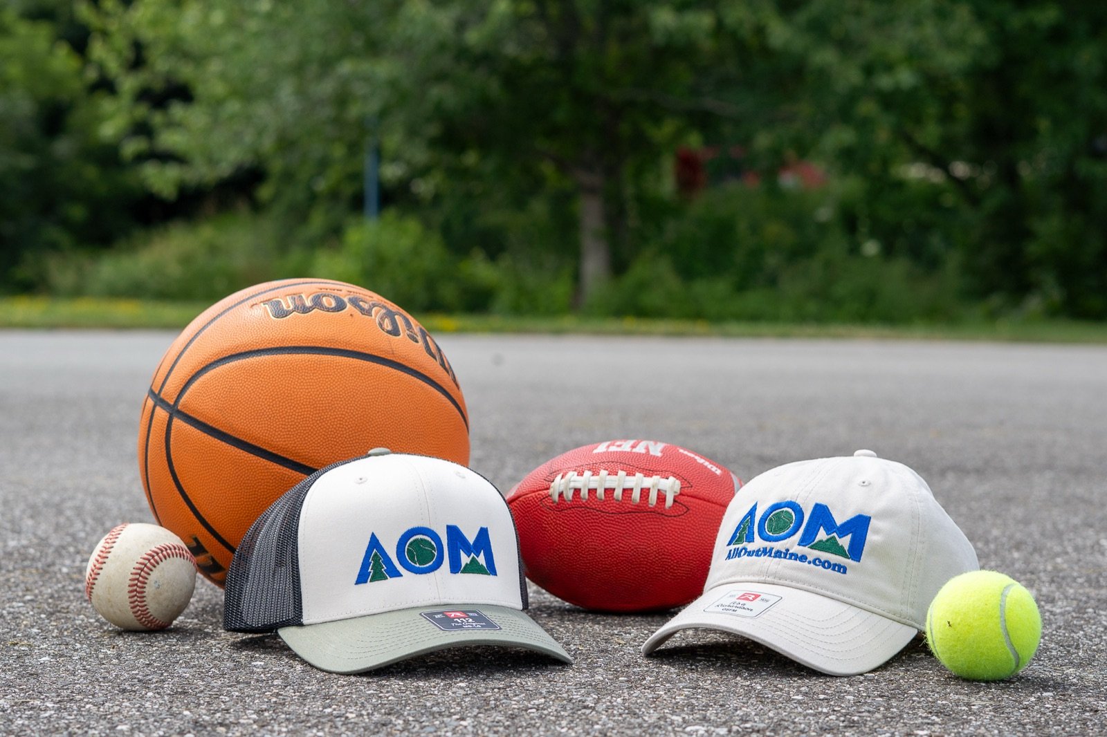 AllOutMaine trucker cap and dad hat on a Maine basketball court, with a basketball, football, baseball and tennis ball